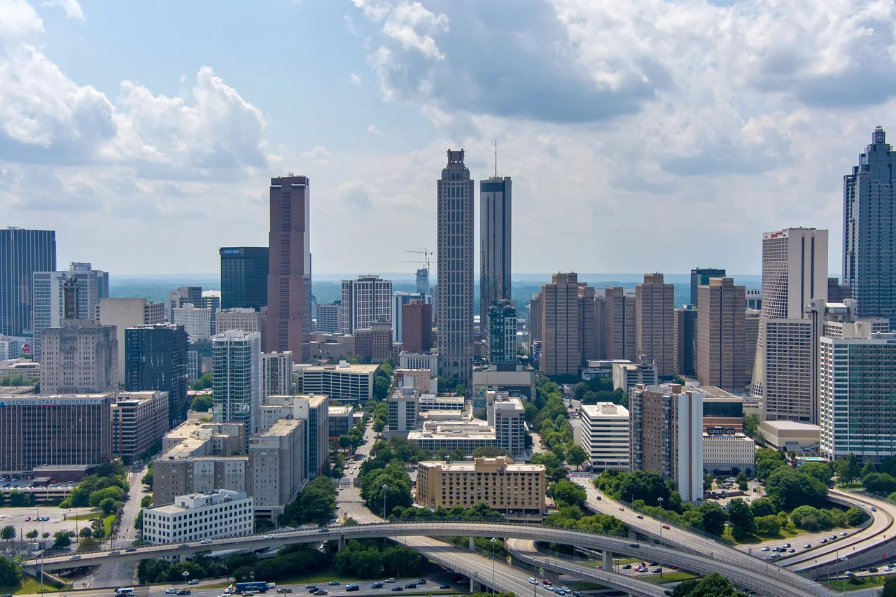 Downtown Atlanta skyline beneath a cloud-filled blue sky with freeway interchanges in the foreground