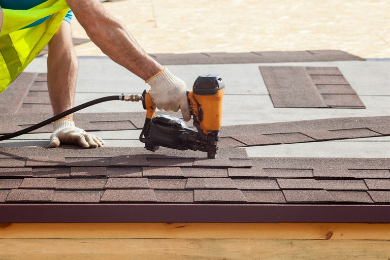 Roofer fastening asphalt shingles with a nail gun