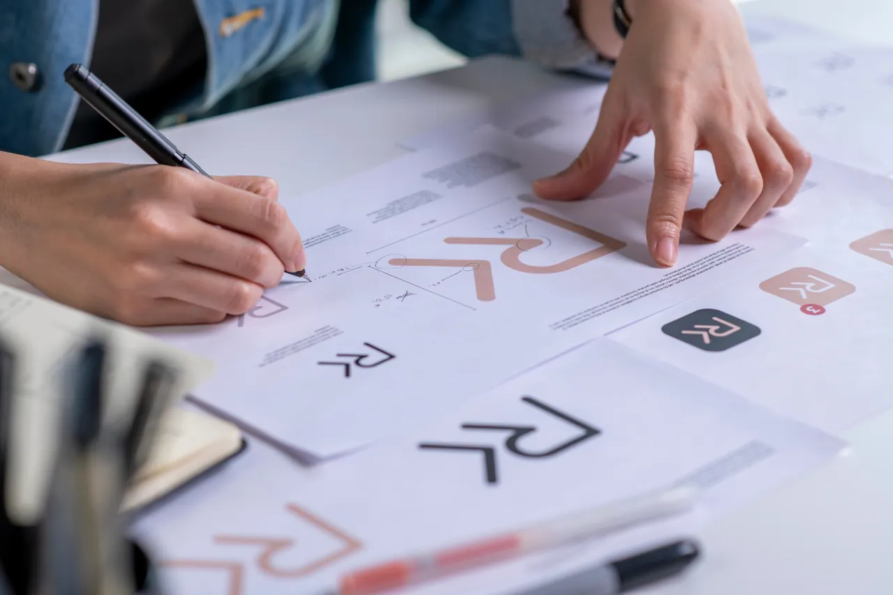 Designer sketching and comparing logo concepts on printed sheets