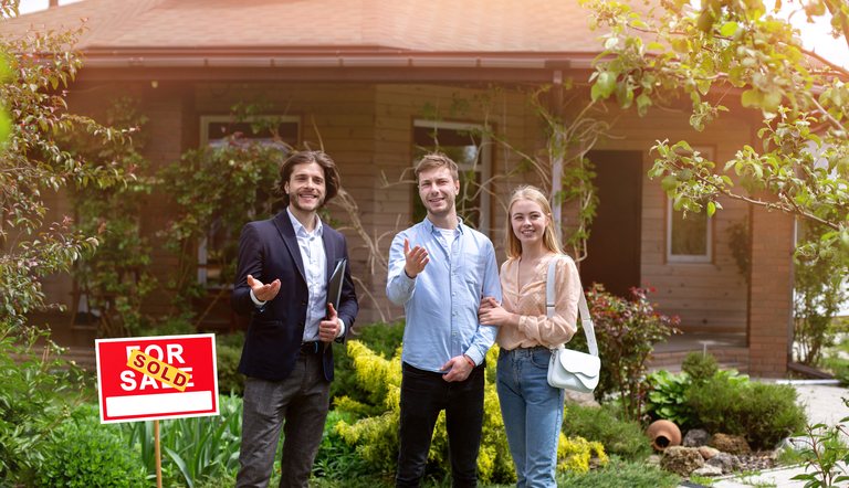 Real estate agent standing with homebuyers outside a sold house