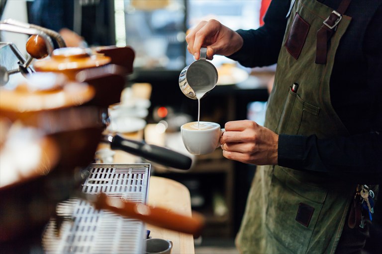 Barista pouring steamed milk into a cup of coffee