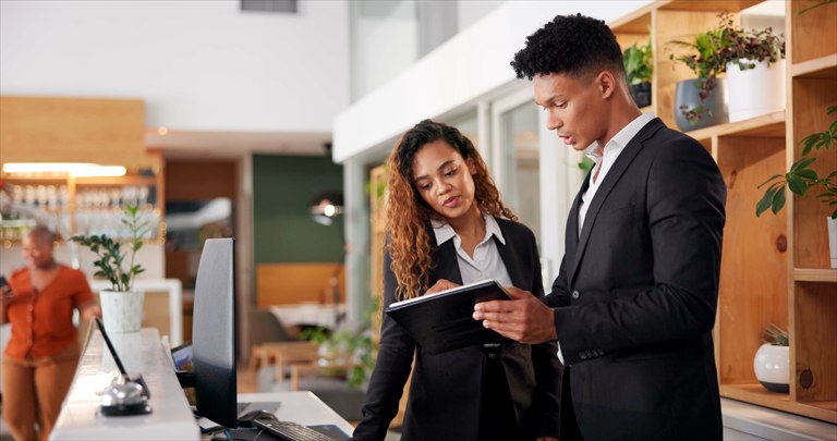 Two hospitality managers reviewing a tablet at a reception desk