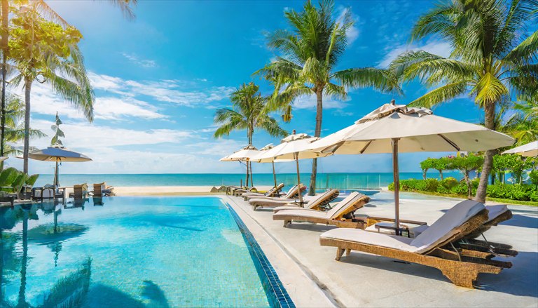 Resort pool with lounge chairs, umbrellas and palm trees beside the ocean