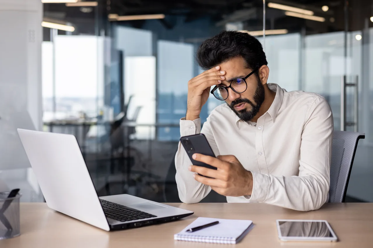 Businessperson checking a smartphone beside an open laptop